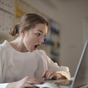 Surprised woman sitting at desk with laptop indoors, expressing amazement.